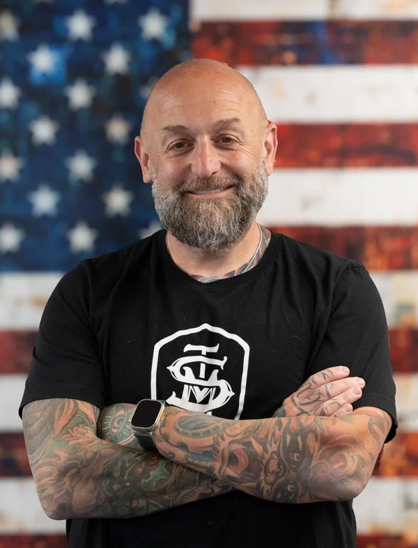 Dave Uziel, CEO of Urban Worldwide, smiling with arms crossed in front of an American flag